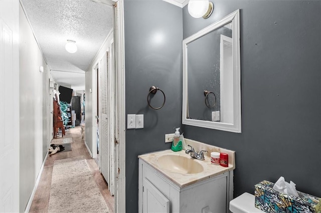 bathroom with baseboards, a textured ceiling, vanity, and toilet