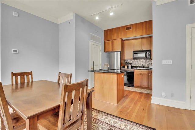 interior space featuring light wood-type flooring, backsplash, track lighting, a kitchen island with sink, and black appliances