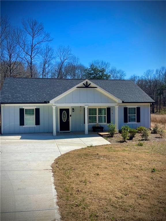 view of front facade with board and batten siding, concrete driveway, roof with shingles, and a front yard