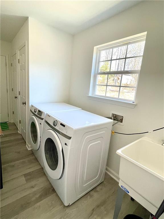 laundry area with laundry area, washing machine and dryer, light wood-type flooring, and a sink