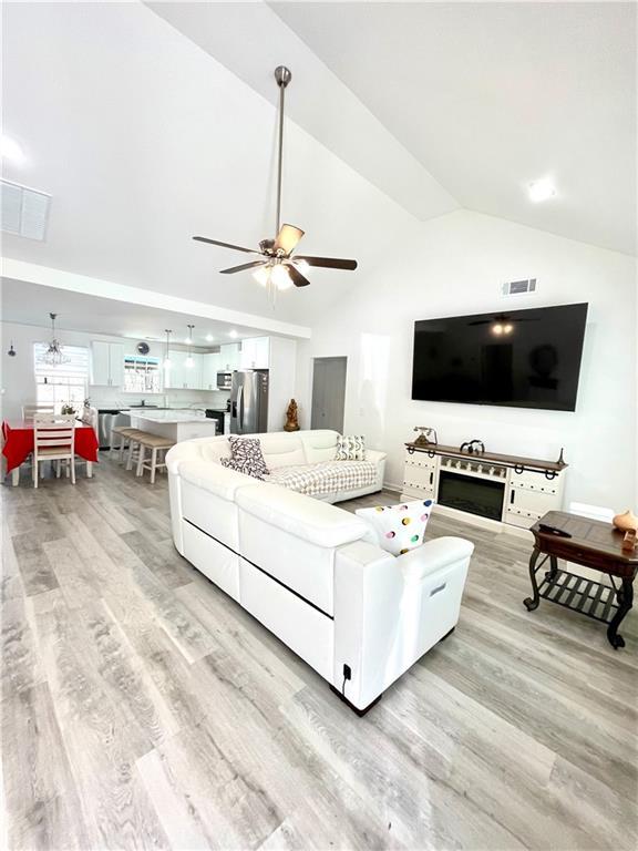 living room featuring visible vents, light wood-style flooring, high vaulted ceiling, and a ceiling fan