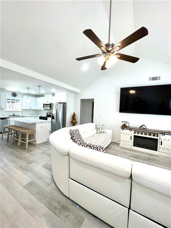 living room featuring light wood-style flooring, visible vents, high vaulted ceiling, and ceiling fan