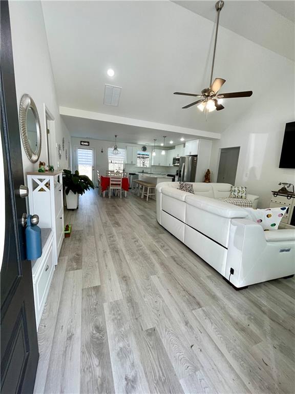 living area with light wood-type flooring, high vaulted ceiling, visible vents, and a ceiling fan