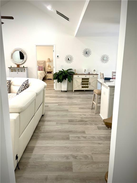 bedroom with light wood-type flooring, wine cooler, high vaulted ceiling, and visible vents