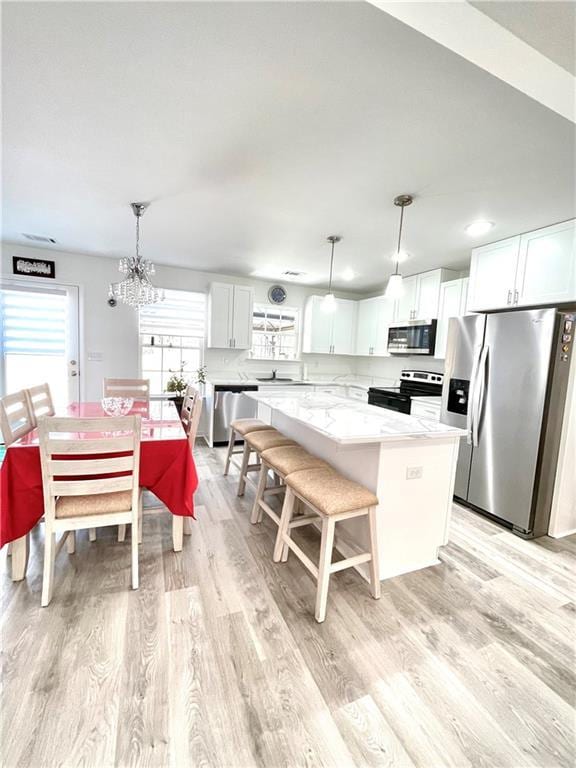 kitchen with light wood-type flooring, a center island, white cabinetry, appliances with stainless steel finishes, and hanging light fixtures