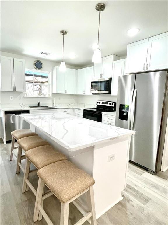 kitchen featuring appliances with stainless steel finishes, a center island, light wood-style floors, and light stone countertops