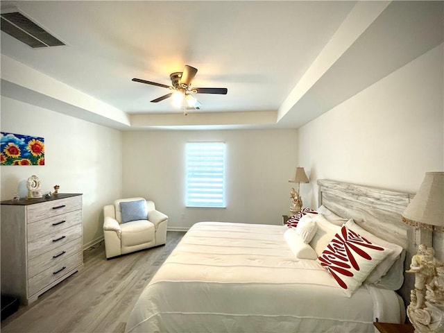 bedroom with visible vents, a raised ceiling, light wood-style floors, and ceiling fan