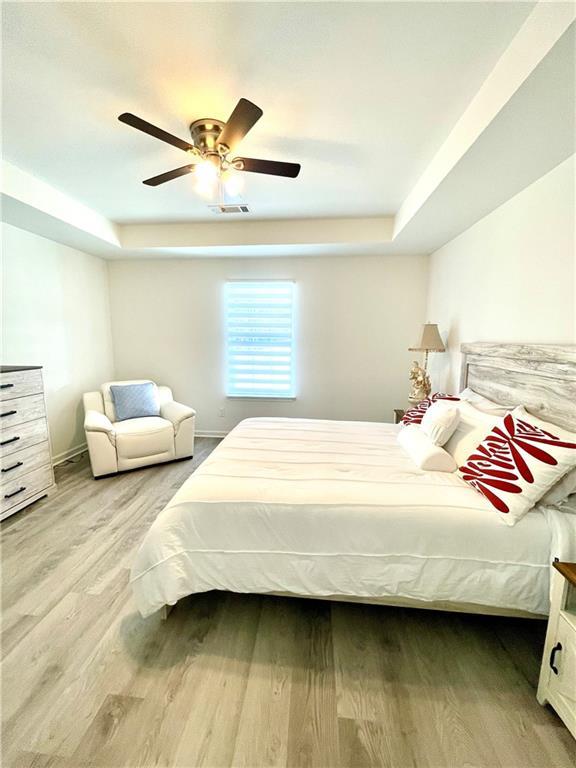 bedroom featuring visible vents, ceiling fan, baseboards, a tray ceiling, and wood finished floors