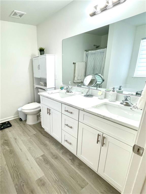 full bathroom featuring visible vents, toilet, a sink, wood finished floors, and a shower