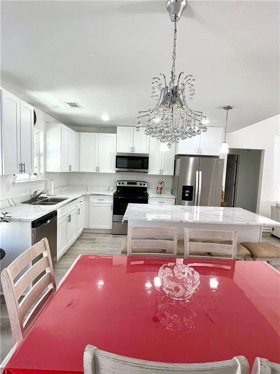 kitchen featuring light wood-style flooring, a sink, appliances with stainless steel finishes, white cabinetry, and a center island