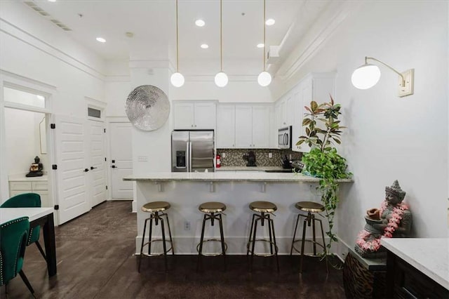 kitchen with backsplash, pendant lighting, white cabinetry, light stone countertops, and appliances with stainless steel finishes