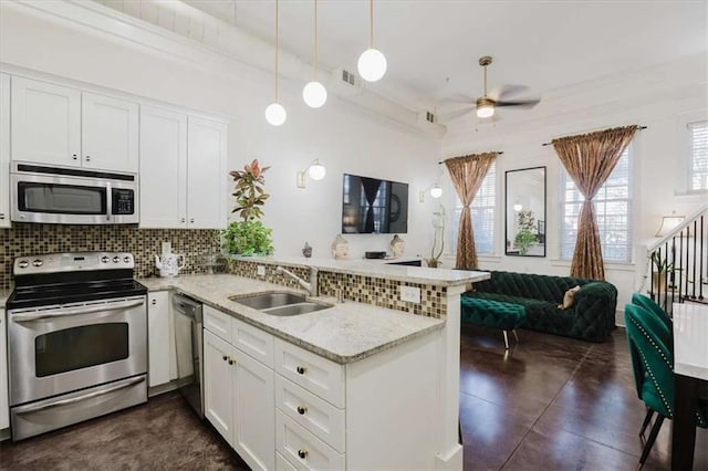 kitchen featuring kitchen peninsula, appliances with stainless steel finishes, hanging light fixtures, white cabinets, and sink