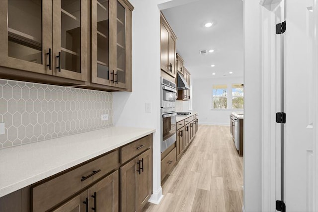 kitchen featuring light hardwood / wood-style floors, exhaust hood, backsplash, and double oven