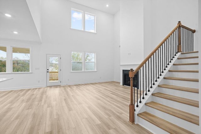 unfurnished living room with light wood-type flooring and a towering ceiling