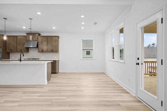 kitchen featuring a wealth of natural light, backsplash, hanging light fixtures, and a kitchen island with sink