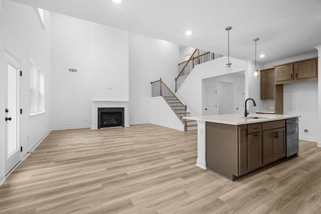 kitchen with dishwasher, a center island with sink, sink, hanging light fixtures, and light wood-type flooring