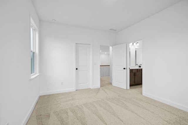 unfurnished bedroom featuring ensuite bathroom, sink, and light colored carpet