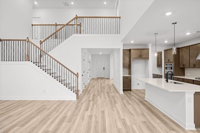 kitchen with stainless steel double oven, a kitchen island with sink, sink, decorative light fixtures, and light hardwood / wood-style flooring