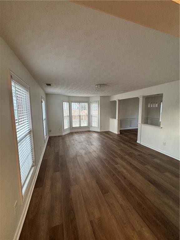 unfurnished living room with baseboards, a textured ceiling, visible vents, and dark wood-type flooring