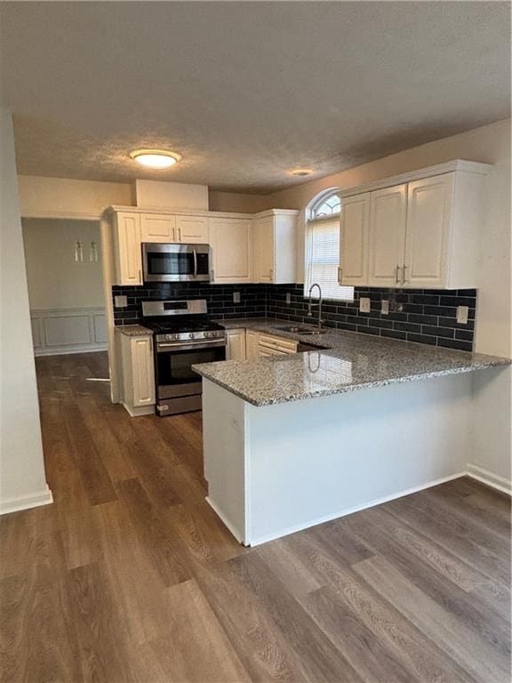 kitchen featuring appliances with stainless steel finishes, white cabinetry, a sink, and a peninsula