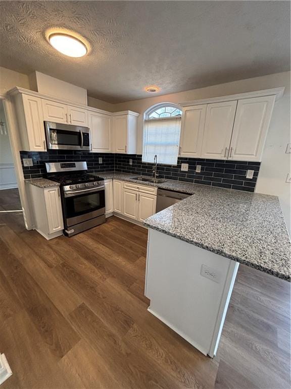 kitchen featuring white cabinets, appliances with stainless steel finishes, a peninsula, light stone countertops, and a sink