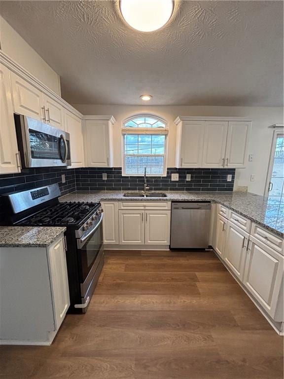 kitchen with light stone counters, appliances with stainless steel finishes, white cabinetry, a sink, and wood finished floors