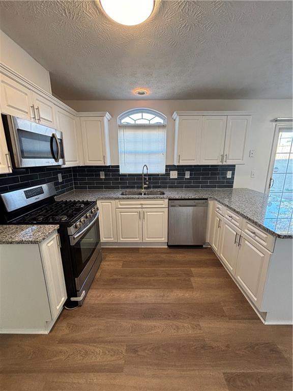 kitchen featuring dark wood-style floors, appliances with stainless steel finishes, stone countertops, white cabinetry, and a sink