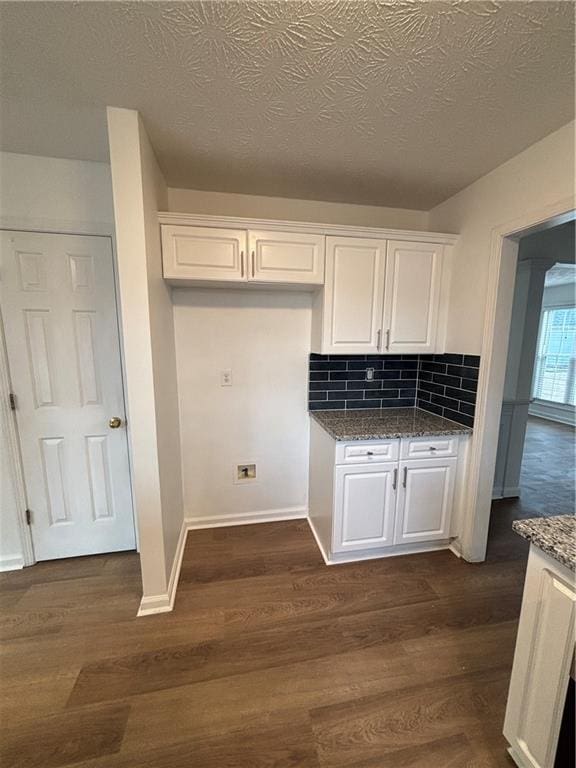 kitchen with baseboards, decorative backsplash, dark stone counters, dark wood finished floors, and white cabinetry