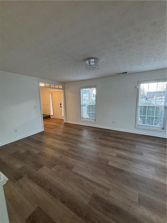 empty room featuring dark wood-type flooring, visible vents, plenty of natural light, and a textured ceiling