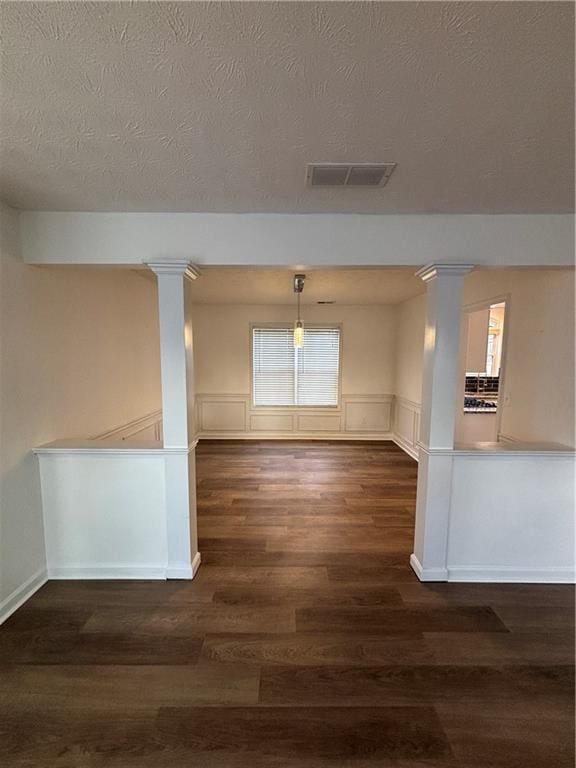 spare room featuring dark wood finished floors, visible vents, and decorative columns