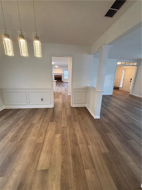 empty room featuring decorative columns, visible vents, and dark wood-style flooring