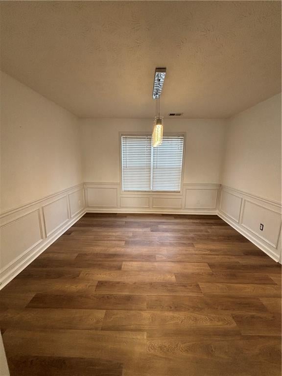 unfurnished dining area featuring dark wood-style flooring, visible vents, and a textured ceiling