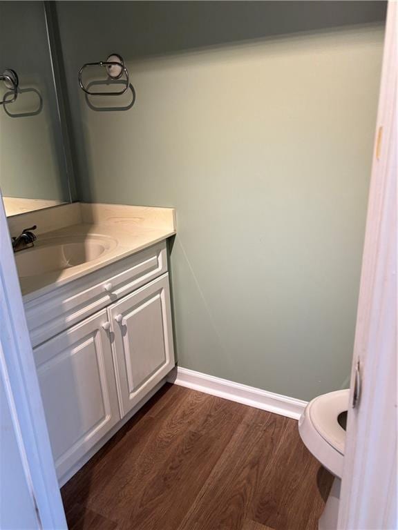 bathroom with toilet, wood finished floors, vanity, and baseboards