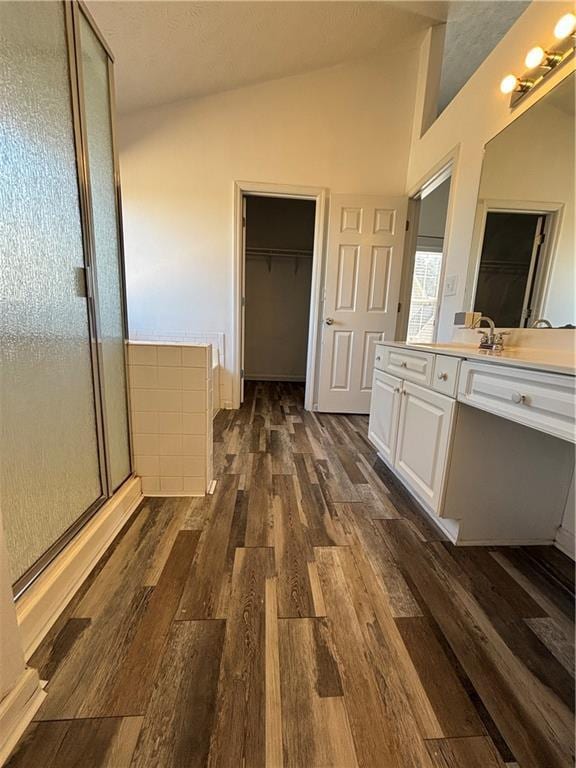 bathroom featuring lofted ceiling, wood finished floors, vanity, a spacious closet, and a shower stall