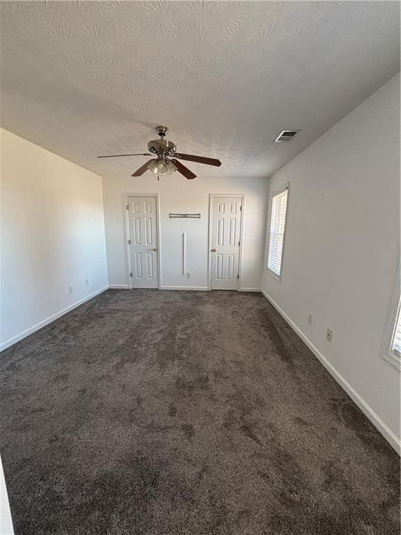 interior space with a textured ceiling, a ceiling fan, visible vents, baseboards, and dark carpet