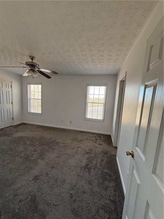 unfurnished room featuring baseboards, dark colored carpet, and a textured ceiling