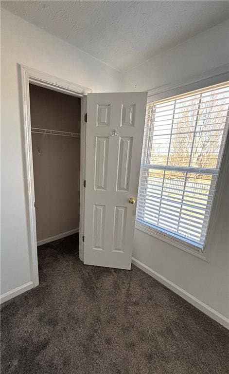 unfurnished bedroom with a textured ceiling, multiple windows, dark carpet, and baseboards