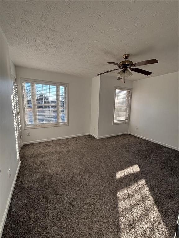 empty room with a ceiling fan, baseboards, dark carpet, and a textured ceiling