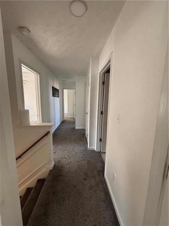 hall with dark colored carpet, a textured ceiling, and baseboards