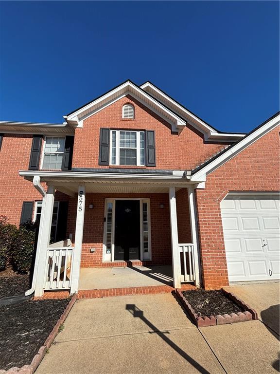 traditional-style house featuring a garage, a porch, and brick siding