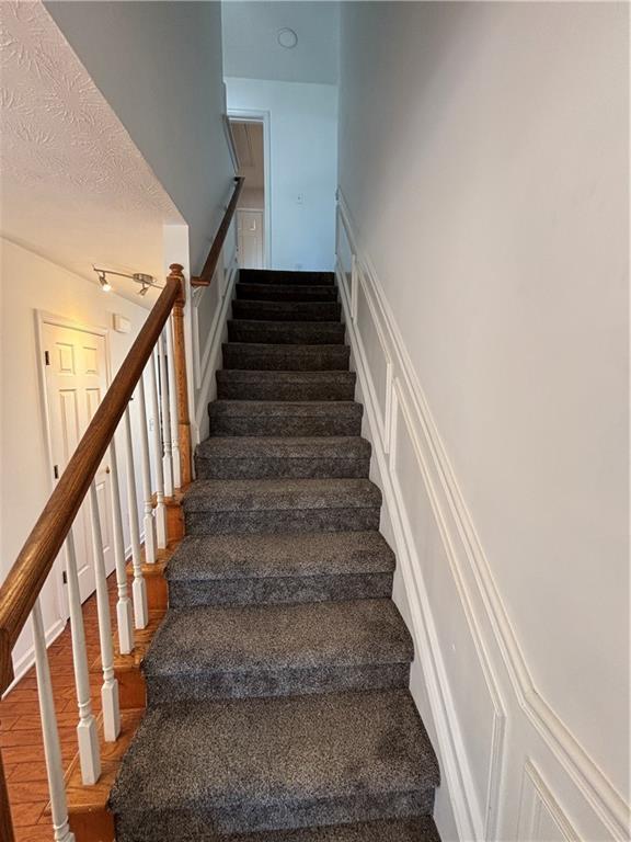 stairs featuring track lighting, a decorative wall, a textured ceiling, and wood finished floors