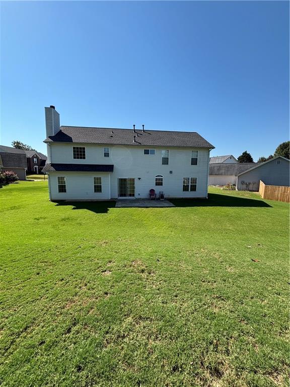 rear view of house featuring a yard, a chimney, and fence