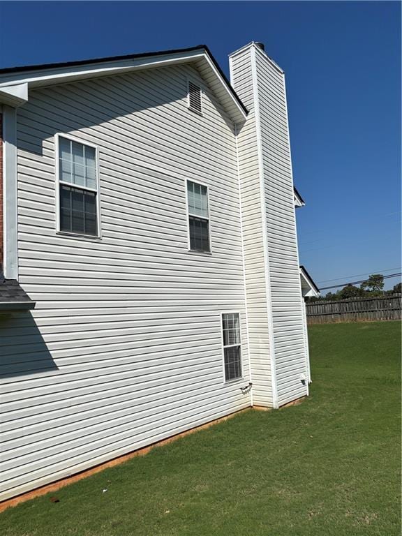 view of side of home featuring a lawn, a chimney, and fence