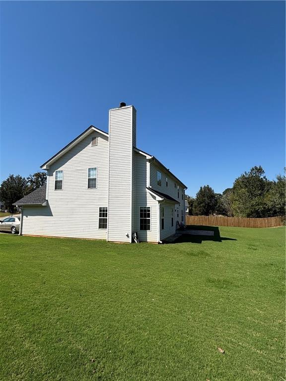 rear view of house with fence, a chimney, and a lawn