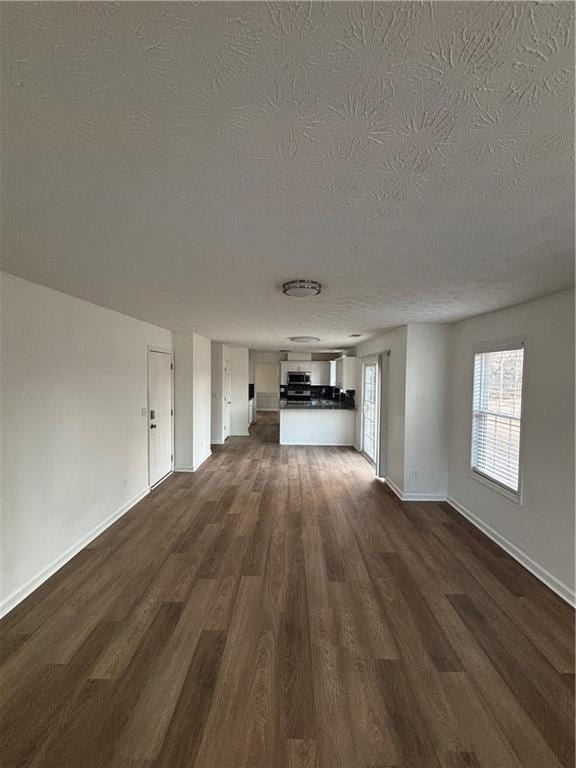 unfurnished living room featuring a textured ceiling, dark wood-type flooring, and baseboards