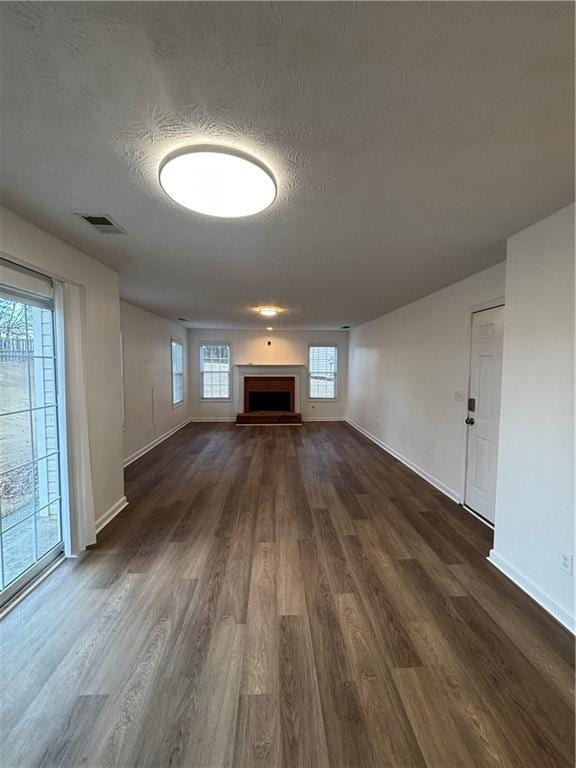 unfurnished living room with dark wood-style floors, a fireplace with raised hearth, visible vents, a textured ceiling, and baseboards