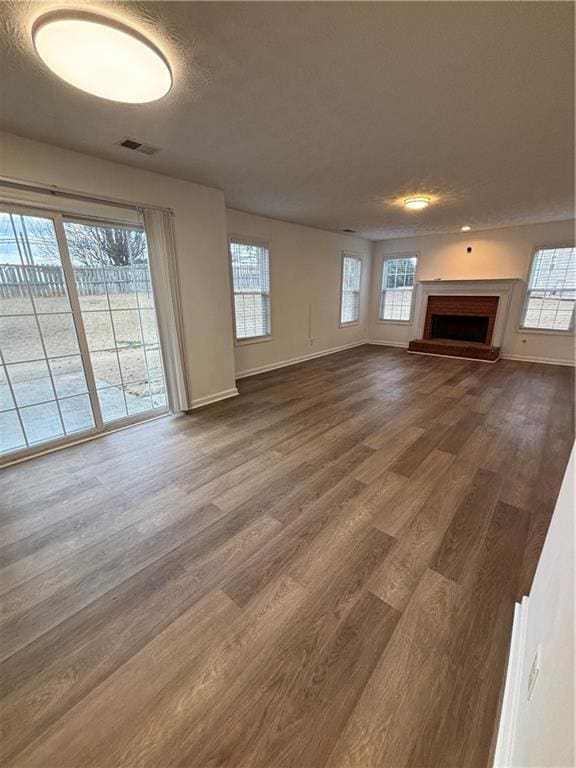 unfurnished living room featuring dark wood-type flooring, a brick fireplace, visible vents, and a healthy amount of sunlight