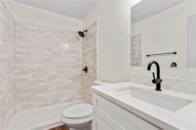 bathroom with tiled shower, vanity, and toilet