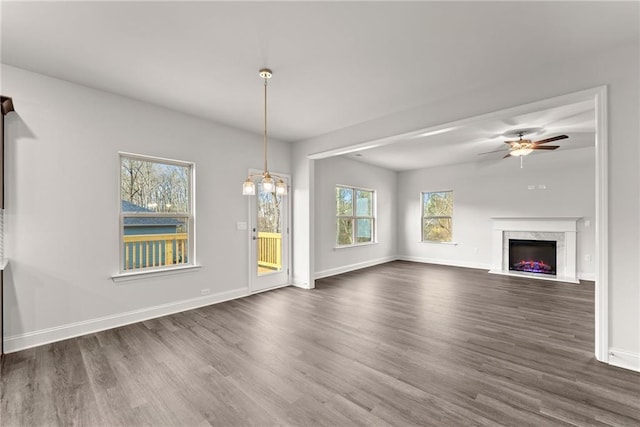 unfurnished living room featuring dark wood-type flooring, ceiling fan with notable chandelier, baseboards, and a premium fireplace