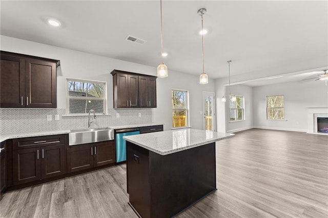 kitchen with stainless steel dishwasher, a glass covered fireplace, open floor plan, a sink, and dark brown cabinets